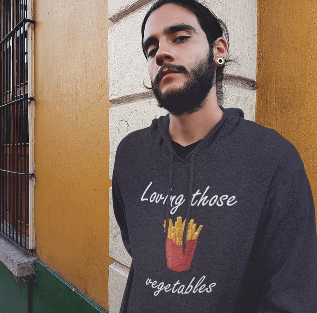 young hipster guy with a beard wearing a pullover hoodie while leaning on a yellow wall